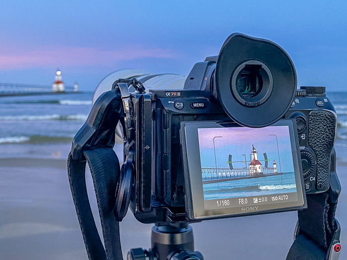 A Mirrorless Sony camera on a tripod photographing a beach and lighthouse at sunrise