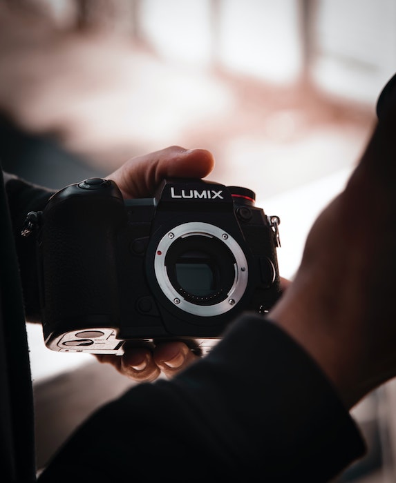 A person holding a Lumix brand camera body with one hand