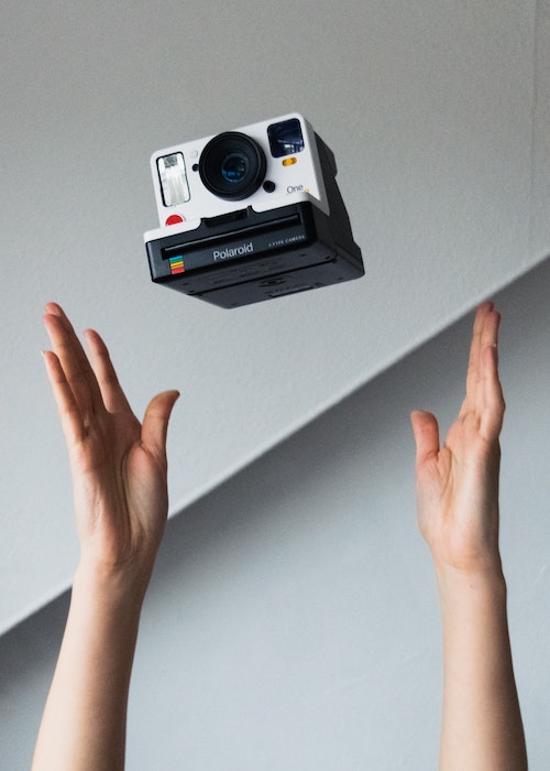 A person tossing a Polaroid camera brand automatic camera in the air