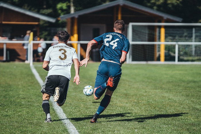 two footballers run down the sideline chasing after the ball