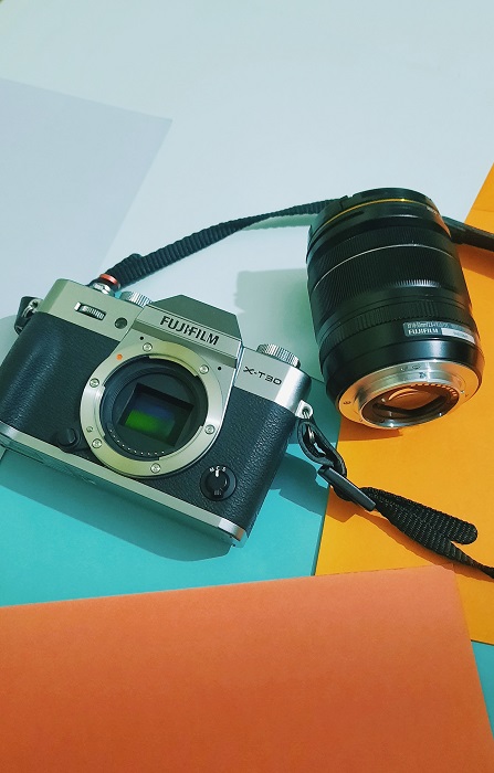 a Fujifilm XT-30 and a lens atop a colorful flat-lay background