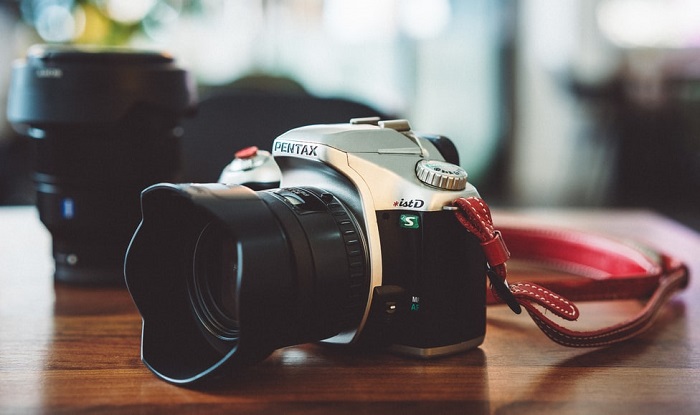 a Pentax DSLR sits atop a wooden table 