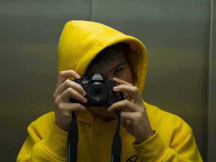 someone in a yellow hoodie points a camera at the photographer taking this photo