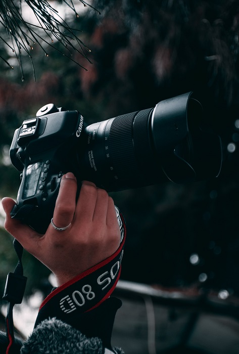 a photographer holds a DSLR with a large lens in a forest