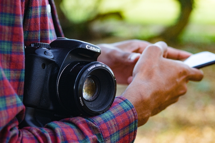 Person cradling a Canon camera and researching fujifilm vs canon on smartphone 