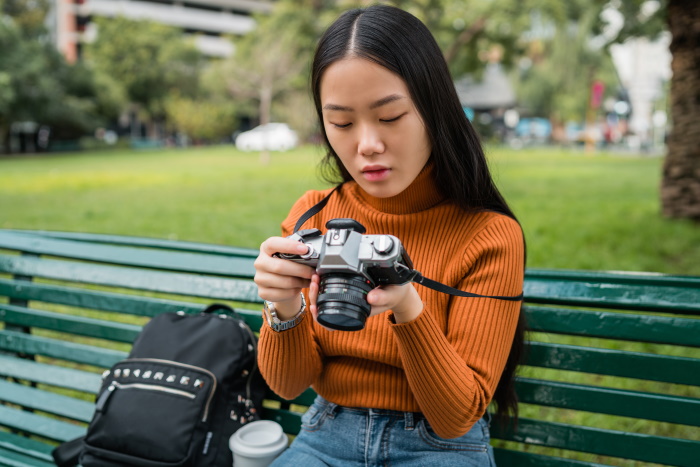 A female photographer adjusting a touchscreen camera on a park bench outdoors