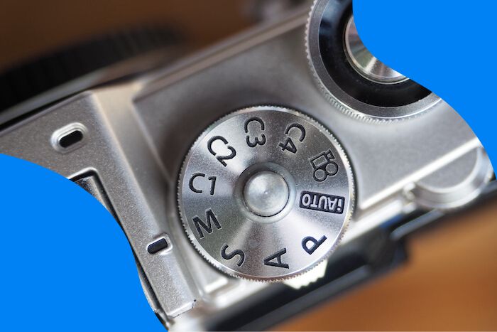 Dial mode and shutter button on silver mirrorless camera.