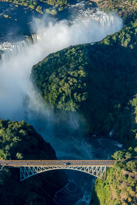 Aerial shot of Victoria Falls, forest trees, and a bridge with vehicles on it